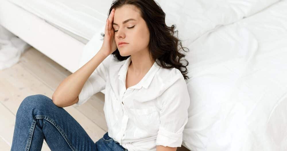 Women touching her head in pain while sitting on the floor