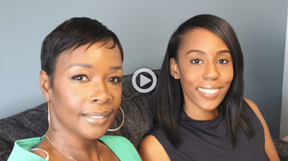 Two women sitting on a couch with one wearing a green shirt and hoop earrings and the other dressed in a dark blue sleeveless top.